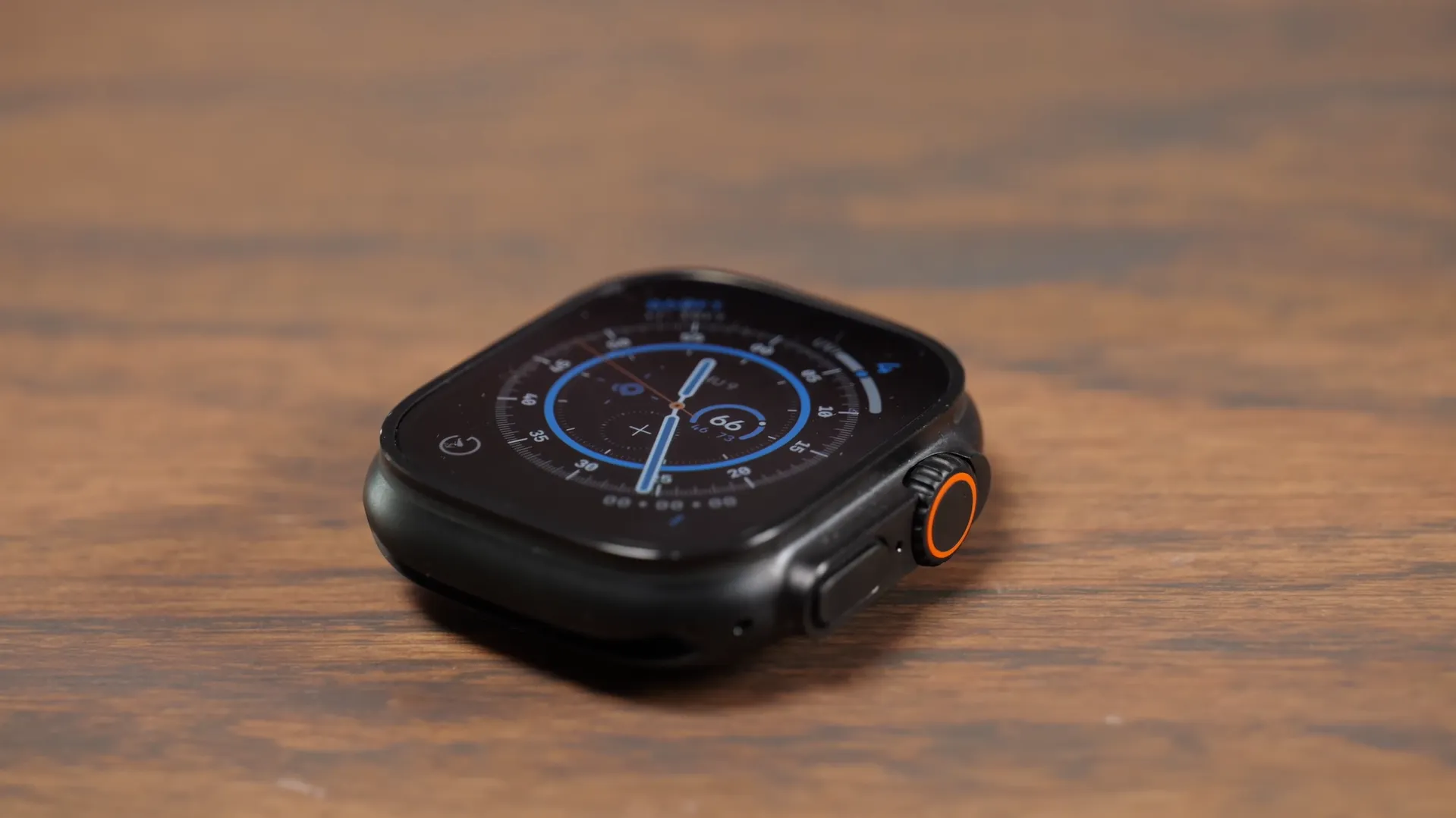 Carcasa masivă din titan negru a Apple Watch Ultra 3 de 49mm așezată plan pe o masă