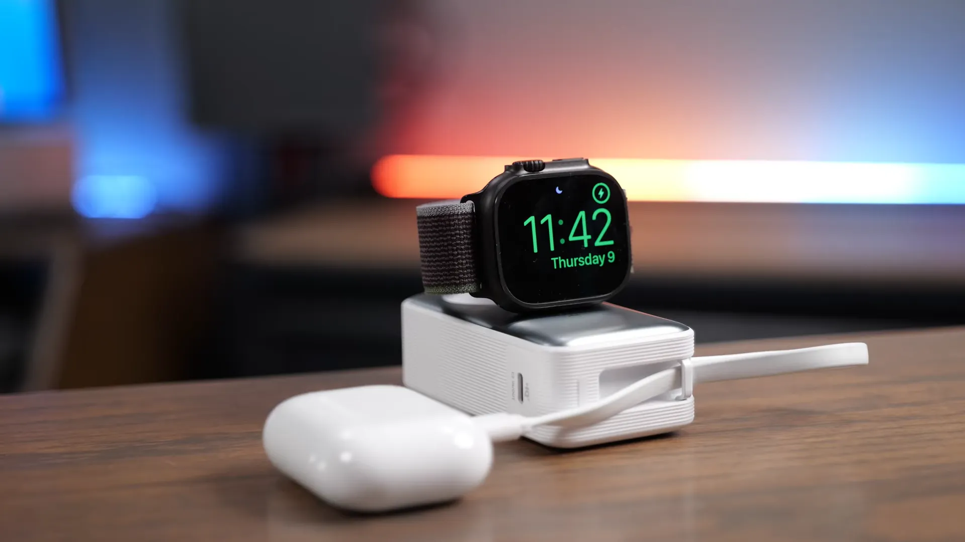 Apple Watch Ultra 3 încărcându-se pe o baterie externă de voiaj, cu o carcasă de AirPods alături