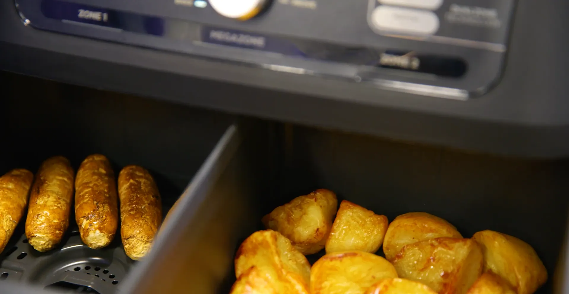 Friteuză Ninja Foodi gătind simultan cârnați într-o zonă și cartofi prăjiți în cealaltă zonă separată