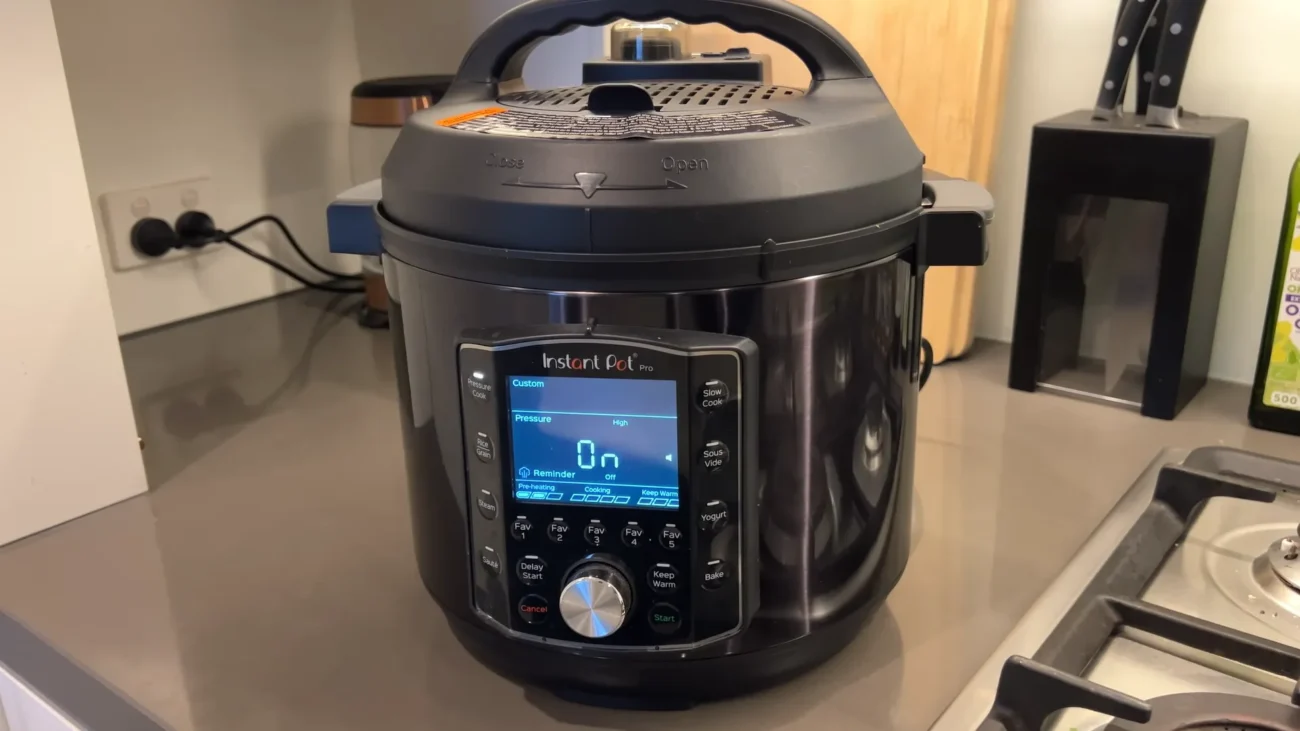 Multicooker Instant Pot Pro 8 așezat pe blatul de bucătărie, cu ecranul digital pornit afișând gătirea sub presiune