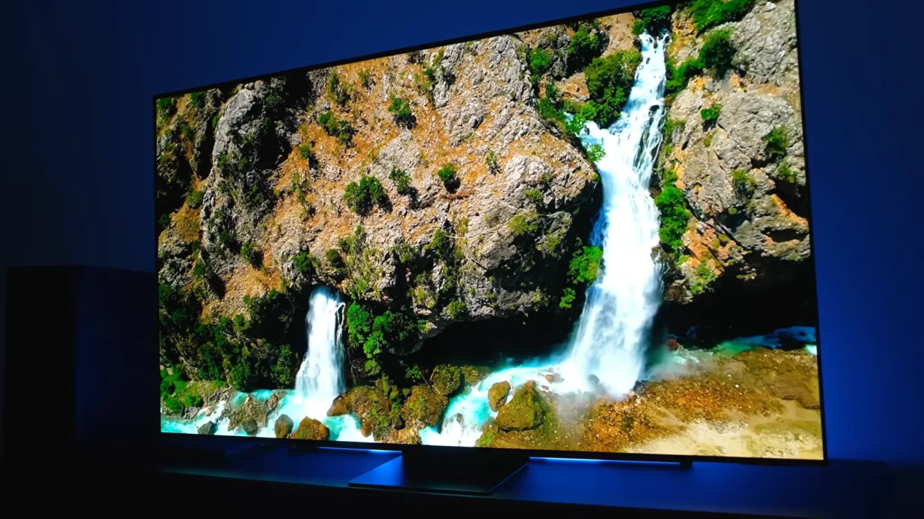 Televizor Samsung OLED 55S95F vizionat într-o cameră întunecată, redând o cascadă luminoasă cu negru perfect pe fundal
