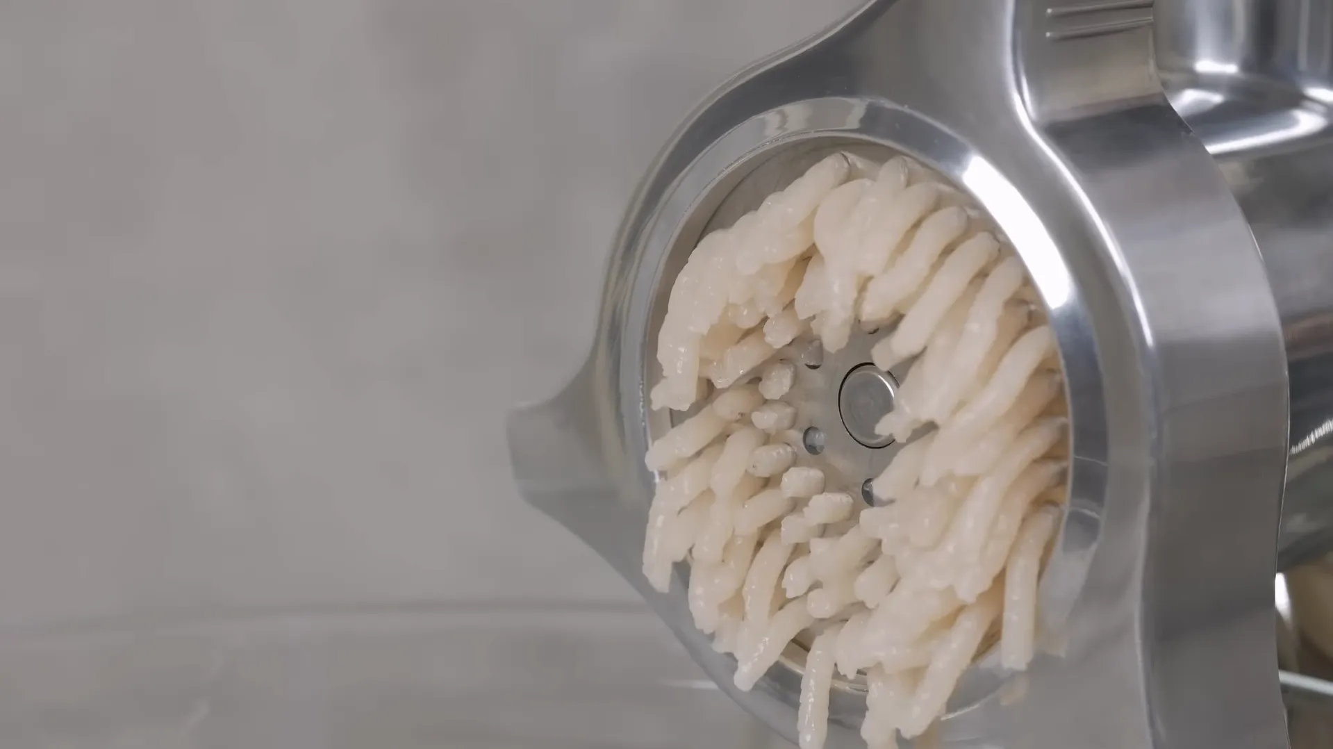 Prim-plan cu pasta de carne fiind extrudată curat prin sita din oțel inoxidabil a mașinii Bosch MFW67440