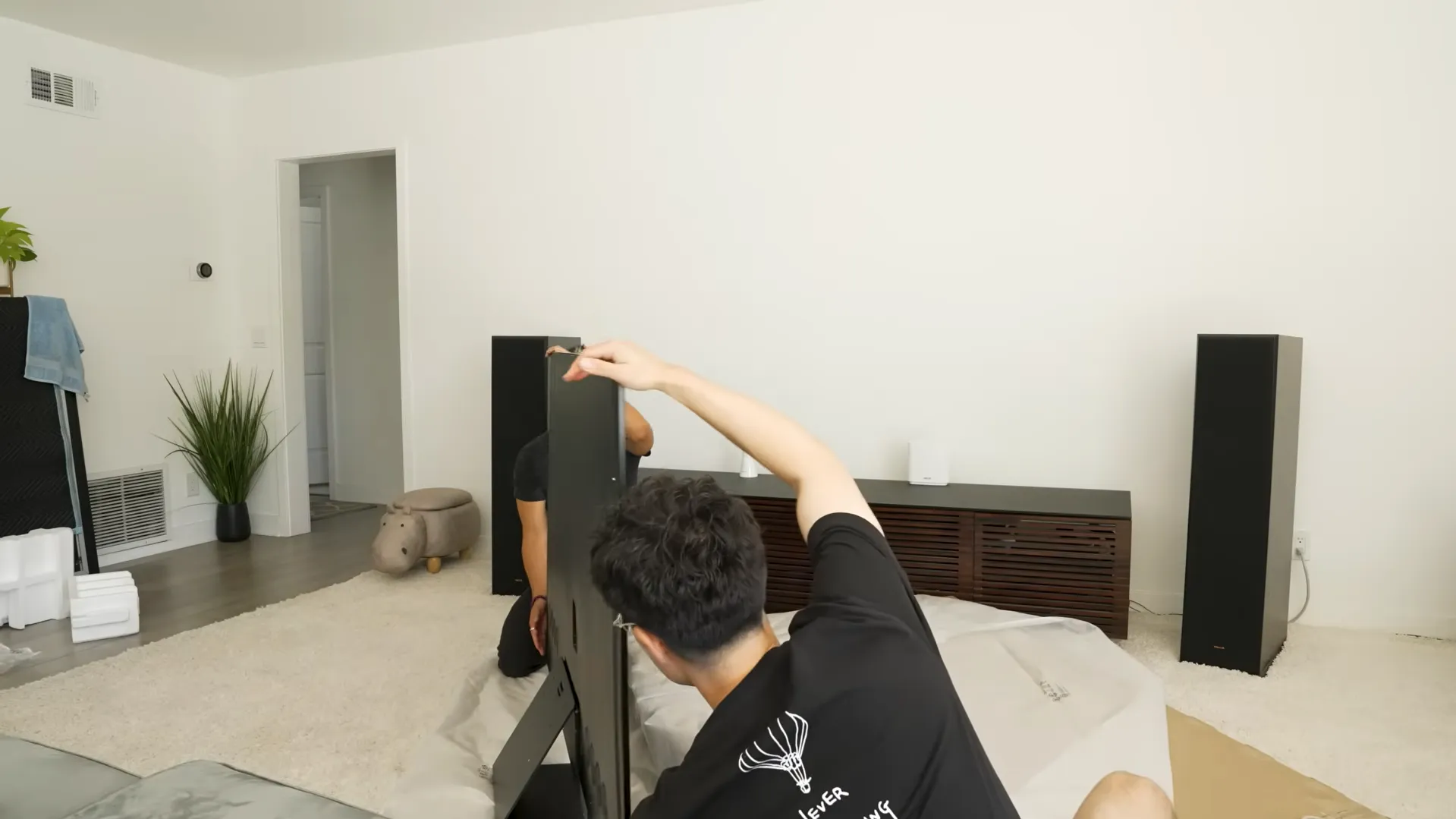 Doi bărbați montând piciorul standului pe un televizor Samsung OLED 55S95F în sufragerie