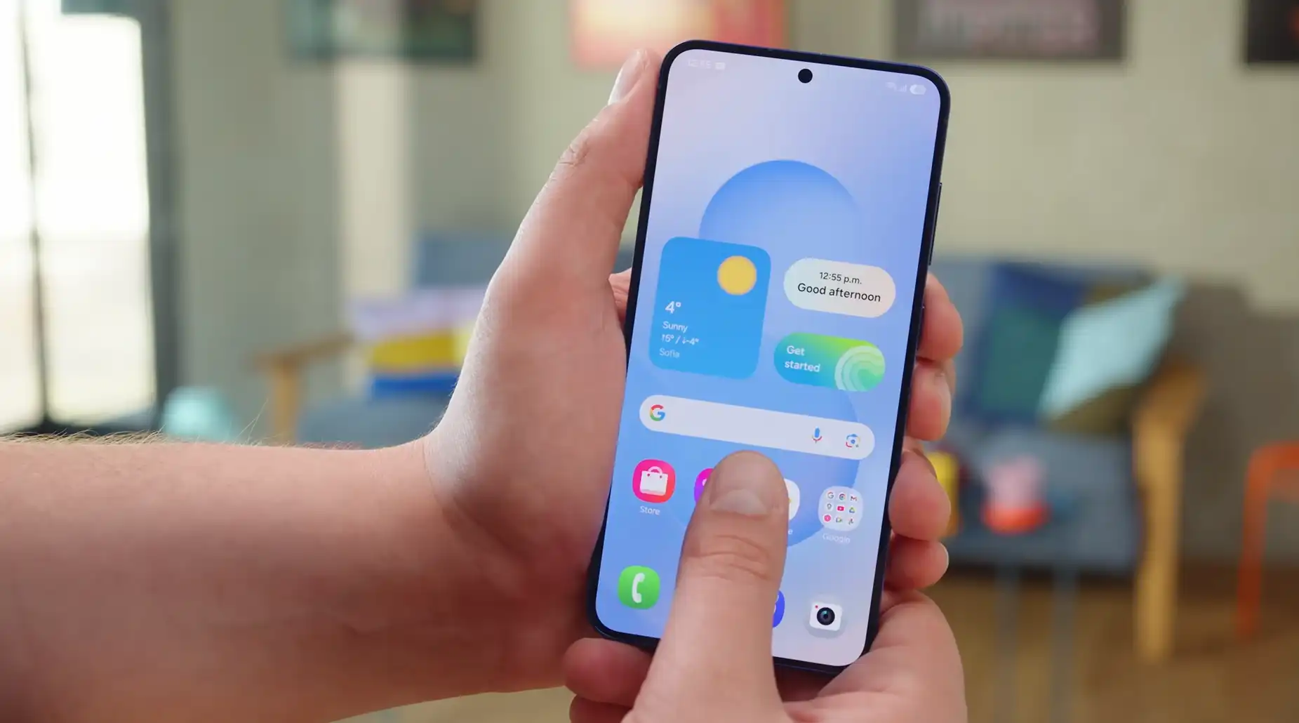 Samsung Galaxy S25 ținut în mână, afișând ecranul de pornire luminos și interfața One UI cu widget-uri